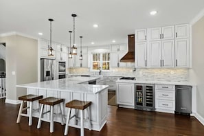 A modern kitchen with white cabinetry, a large island with stools, stainless steel appliances, and pendant lighting. - Waterfront Retreat Lakefront Game Room Dock (Bumpass)