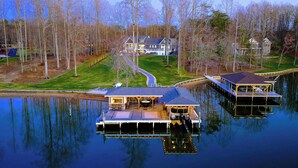 Une maison au bord du lac, dotée d’un quai, d’un espace extérieur aménagé et couvert, et d’un chemin menant à la maison.