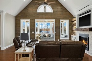 A living room with a fireplace, leather sofas, a ceiling fan, and large windows.