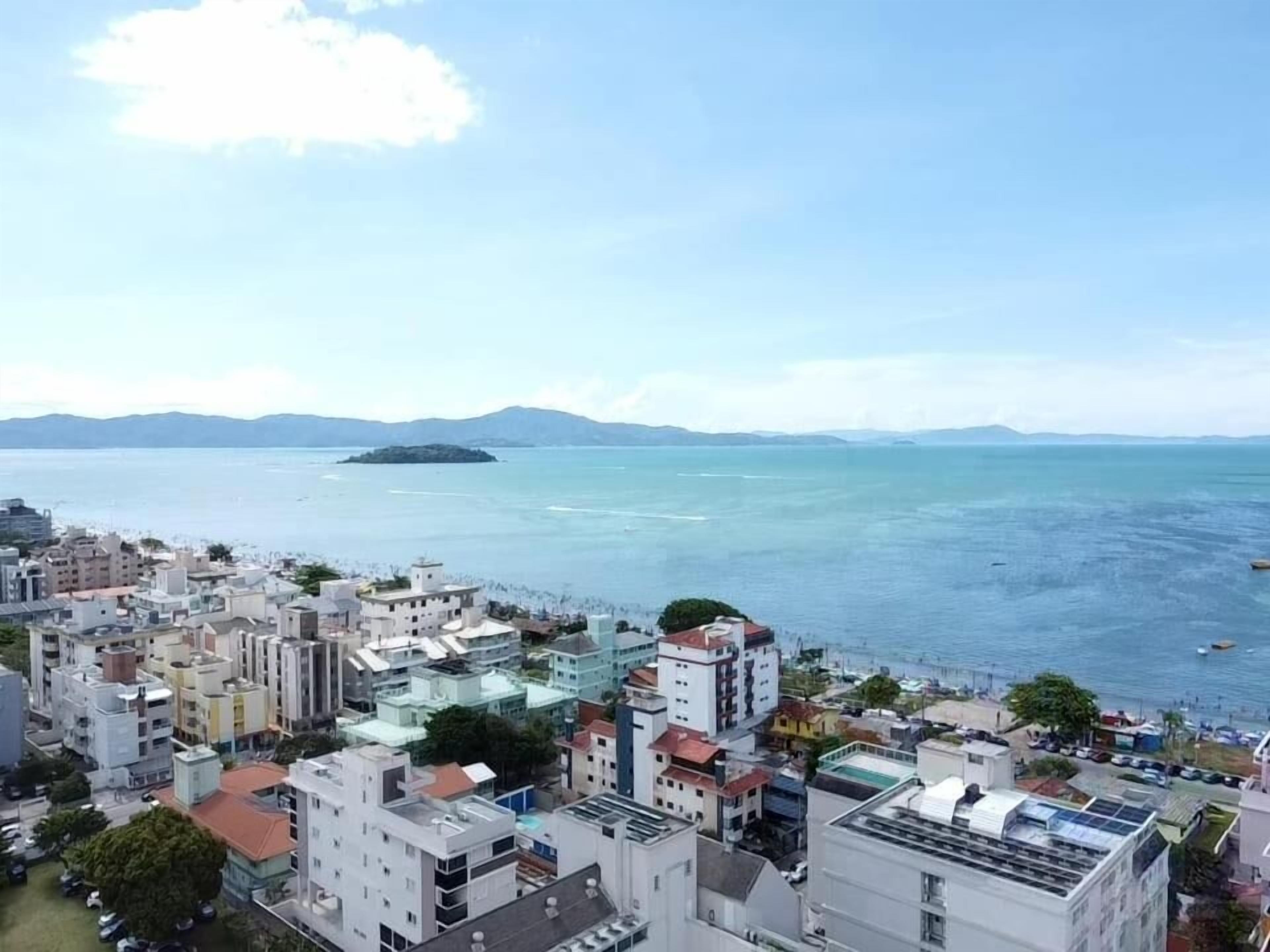 A coastal cityscape with buildings, a body of water, and distant mountains.
