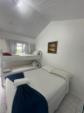 Quarto com cama de solteiro, uma cama individual, janela com cortinas e um quadro na parede.