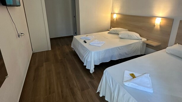 A hotel room with two beds, a ceiling fan, a TV mounted on the wall, and a wooden floor. - Pousada santa Barbara (Florianópolis)