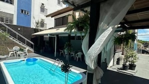 A swimming pool with a pergola, outdoor seating, and a building in the background. - Pousada santa Barbara (Florianópolis)