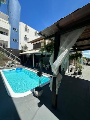 A swimming pool with a pergola, outdoor seating, and a building in the background. - Pousada santa Barbara (Florianópolis)