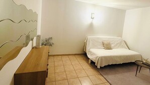 A bedroom with a bed, a wooden dresser, a wall-mounted light, and a tiled floor. - Charming renovated studio 2 steps from the sea - Secure residence with all comforts (Sète)