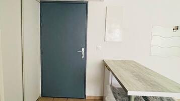 Une pièce avec une porte fermée, un sol carrelé, une table avec une chaise et un luminaire fixé au mur.