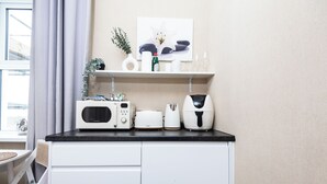 A kitchenette with a microwave, toaster, and coffee maker on a black countertop, above white cabinets. - Bayview Aparthotel by Guestz (Morecambe)
