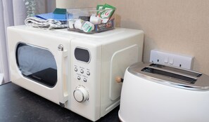 A compact kitchenette with a microwave, toaster, and a small storage container with kitchen items. - Bayview Aparthotel by Guestz (Morecambe)