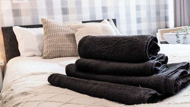 A neatly made bed with rolled towels, a headboard, and a plaid-patterned wall. - Bayview Aparthotel by Guestz (Morecambe)