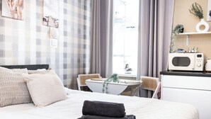 A neatly arranged hotel room with a bed, a desk, a chair, a microwave, and a window with curtains. - Bayview Aparthotel by Guestz (Morecambe)