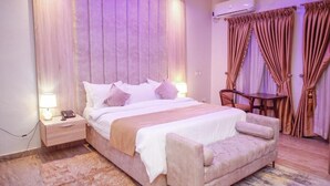 A bedroom with a bed, bedside tables, a nightstand, a chair, a table, and curtains. - The Shortlet Ahvi (Lekki)