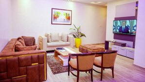 A modern living room with a sofa, chairs, a coffee table, a TV, and a plant. - The Shortlet Ahvi (Lekki)
