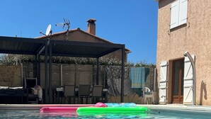 Una piscina cristalina con tumbonas flotantes, una zona de estar cubierta y un edificio con puerta y ventanas.