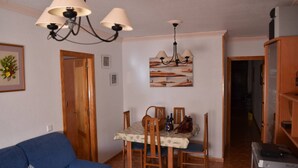 A living room with a blue sofa, a dining table with chairs, a chandelier, and a painting on the wall. - Nice Apartment Near the Beach With Parking and Wifi (Roquetas de Mar)
