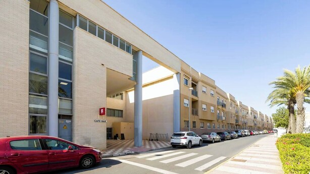 A modern building with a cafe bar, parked cars, and a clear sky. - Nice Apartment Near the Beach With Parking and Wifi (Roquetas de Mar)