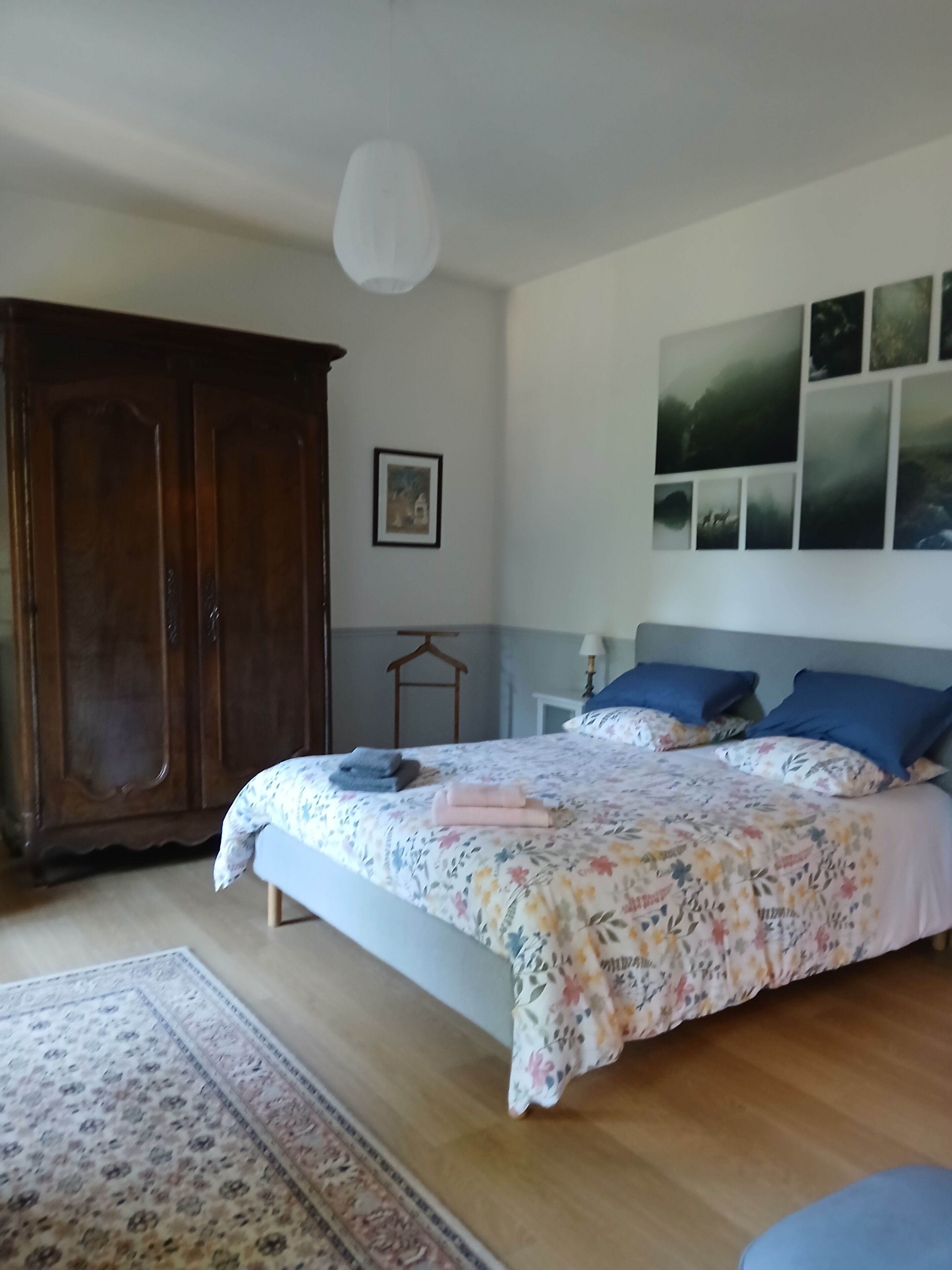Un dormitorio con una cama grande, un armario, un cuadro en la pared y una lámpara colgante.