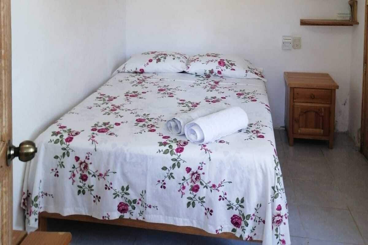 A bedroom with a bed, a ceiling fan, a wooden nightstand, and a wall-mounted shelf.