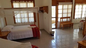 Una habitación con dos camas, un banco de madera, una mesita y una ventana con cortinas.