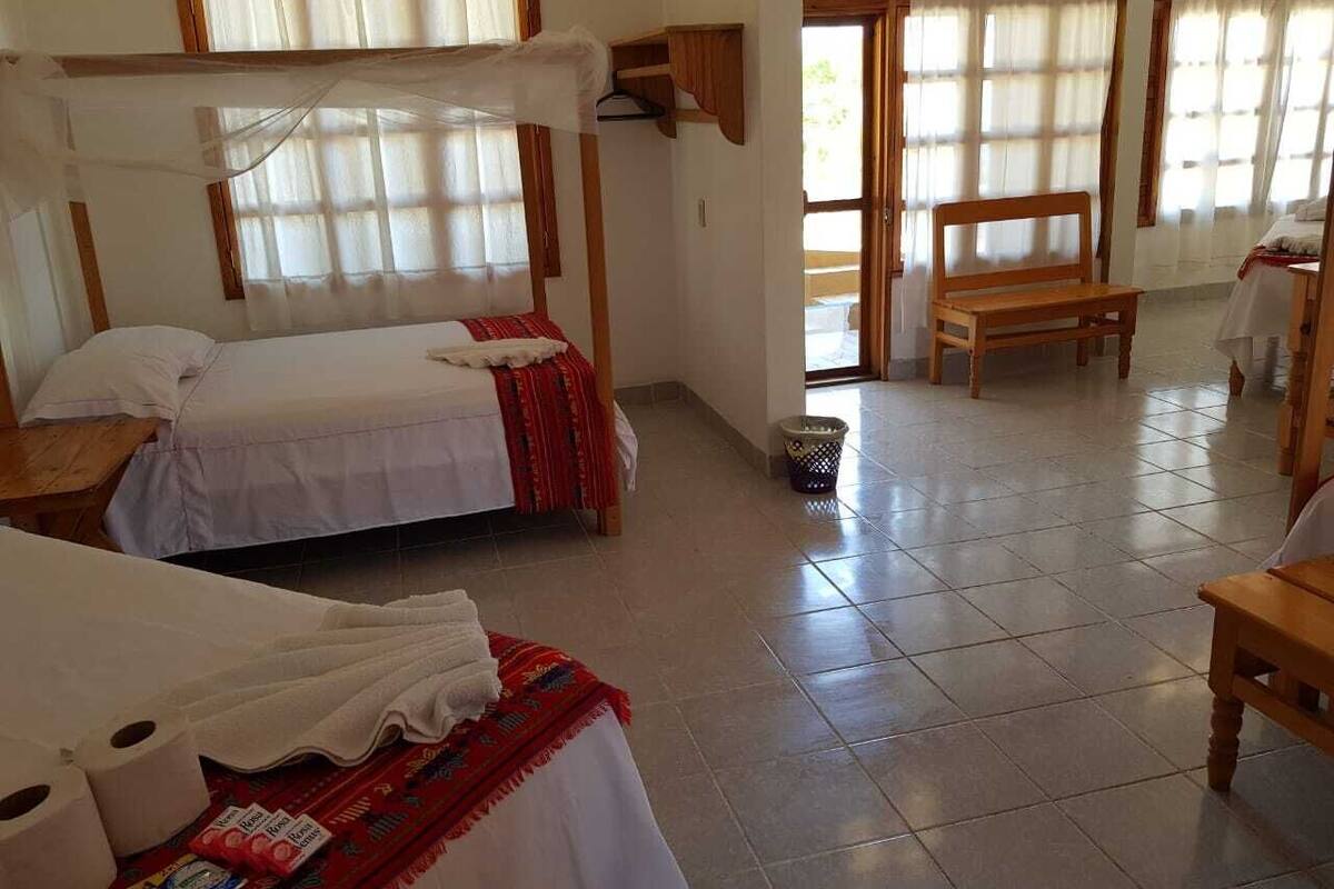 A room with two beds, a wooden bench, a small table, and a window with curtains.