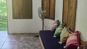 Una habitación con una cama, un ventilador y contraventanas de madera en las ventanas.