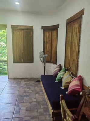 A room with a bed, a fan, and wooden shutters on the windows.