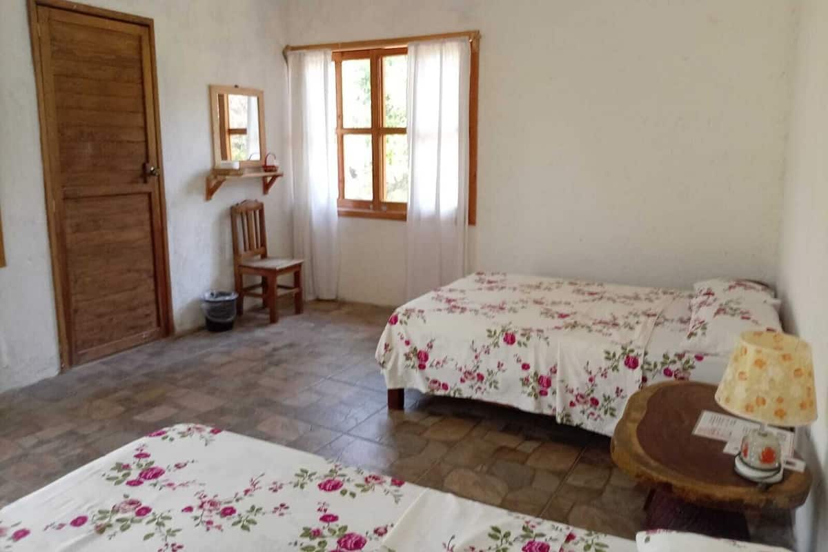 A room with two beds, a wooden door, a chair, a mirror, and a table with a lamp.