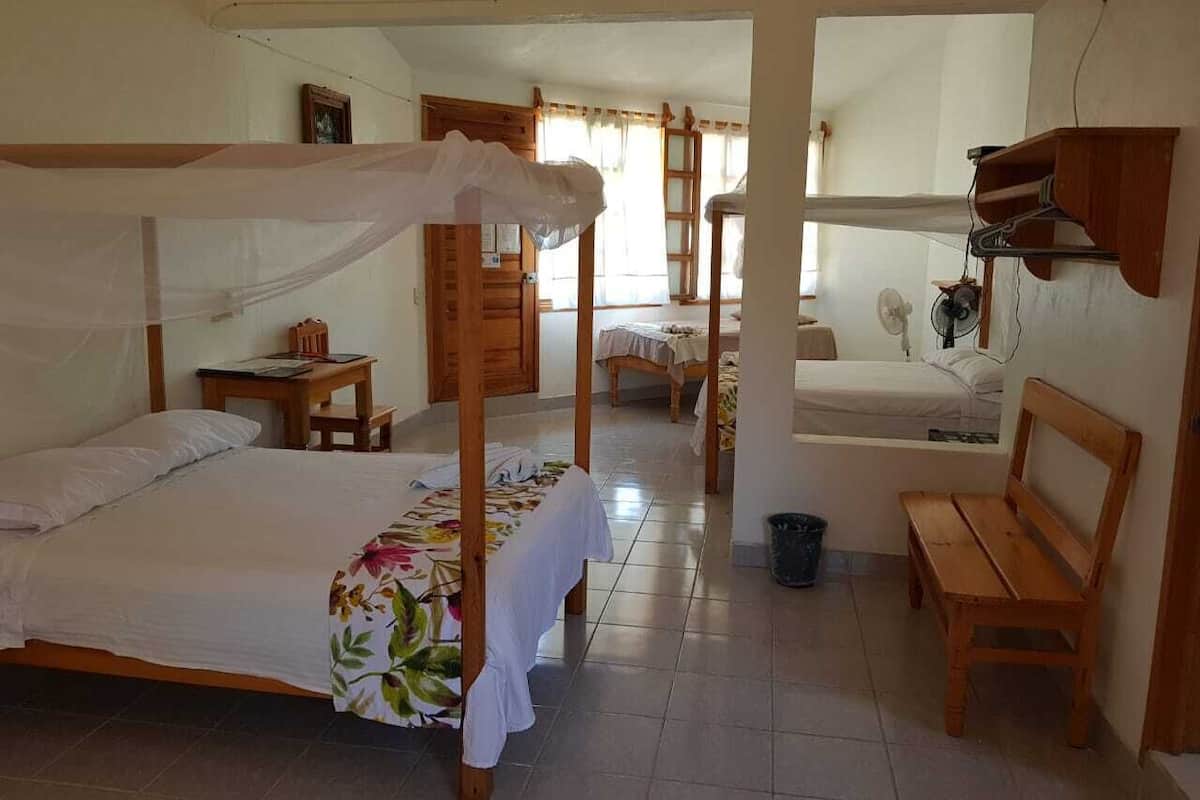 A room with a bed, a wooden bench, a small table, and a fan.