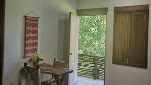 Una habitación con una mesa de comedor, sillas, un tapiz colgante y vistas a la vegetación a través de un umbral abierto.