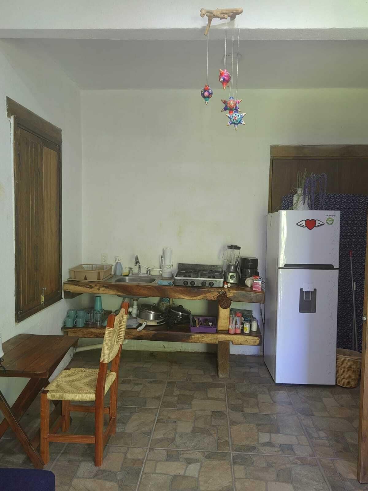 Una cocina con una mesa de madera, una silla, un refrigerador y un adorno colgante.