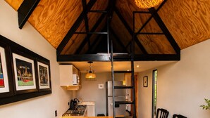 A loft-style room with a wooden ceiling, a loft bed, a kitchenette, a dining area with chairs, and a sofa. - Basecamp A Boutique Cabin Experience in the Wild (Carmen de Carupa)