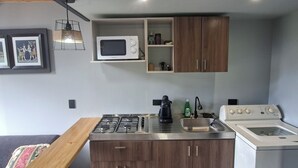 A compact kitchen with a microwave, stove, sink, and a built-in washing machine. - Basecamp A Boutique Cabin Experience in the Wild (Carmen de Carupa)