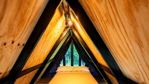 A triangular attic bedroom with a bed, wooden walls, and a patterned rug. - Basecamp A Boutique Cabin Experience in the Wild (Carmen de Carupa)