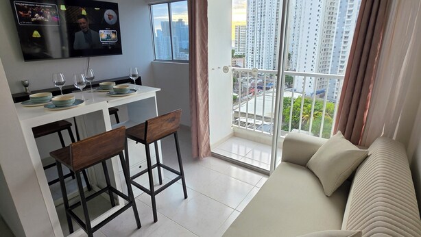 Una sala moderna con sofá, comedor con televisor y balcón con vistas a la ciudad.