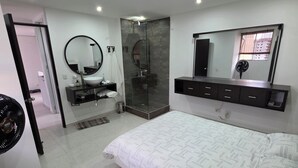 Un dormitorio moderno con una cama grande, un vestidor, un baño con ducha de vidrio y un espejo amplio.