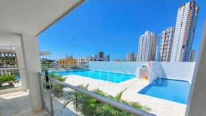 Una piscina en la azotea con agua cristalina, rodeada de palmeras y edificios modernos al fondo.
