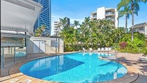 Una piscina con lettini, palme e moderni edifici sullo sfondo.
