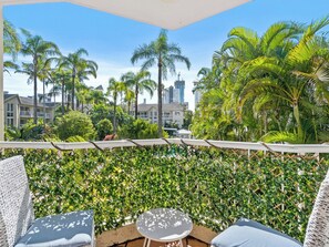 A balcony with a view of palm trees and buildings, a white fence, and outdoor furniture. - Broadbeach Beachside 2BR Pool, Spa, BBQ, Aircon, 2 minute Walk to beach (Gold Coast)