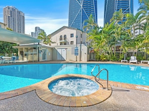 Une piscine avec un jacuzzi, entourée de palmiers et de bâtiments modernes.