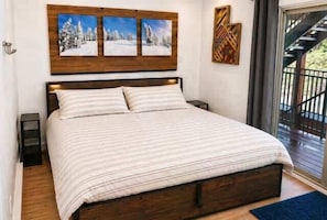 Un dormitorio con cabecera de madera, una cama grande con ropa de cama a rayas, dos cuadros en la pared y vistas a un balcón.