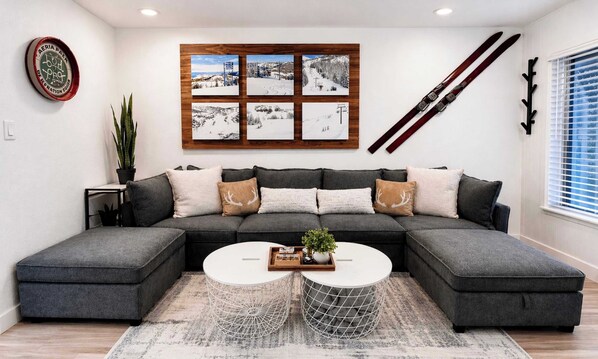 Un salon moderne avec un canapé d’angle, une table basse et un porte-skis fixé au mur.
