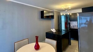 A modern kitchen with a round dining table, chairs, a red vase, a black countertop, and a refrigerator. - 504 ocean tower 60m2 sea view 2 quartos (Fortaleza)