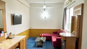 A room with a flat-screen TV, a coffee table with a vase, a sofa, a wooden cabinet, and a window with curtains.