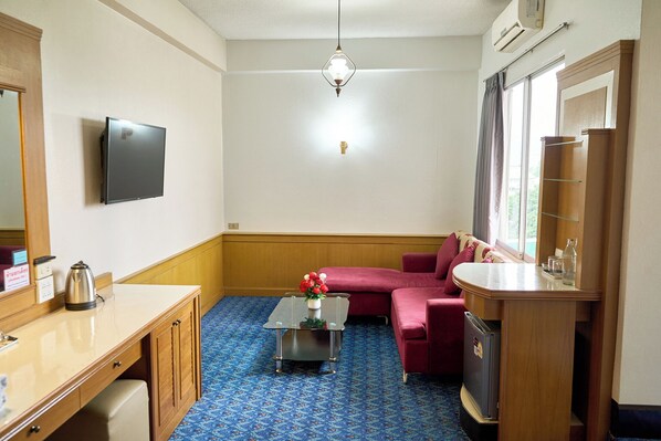 Una habitación con una televisión de pantalla plana, una mesa de centro con un florero, un sofá, un armario de madera y una ventana con cortinas.