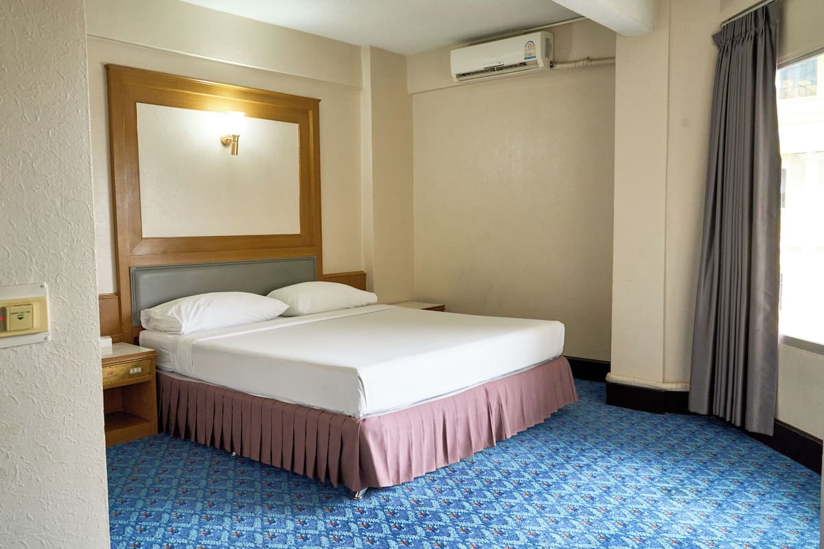 Una habitación de hotel con cama, mesita de noche, aire acondicionado y ventana con cortinas.
