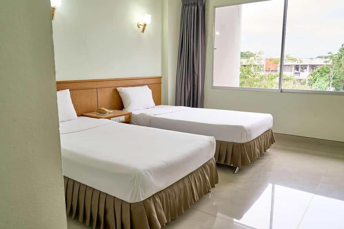 Habitación de hotel con dos camas, una mesita de noche, una lámpara de pared, una ventana con vistas y una cortina.