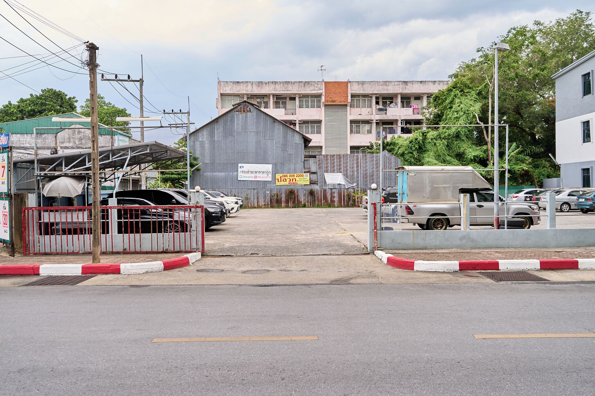 A gated parking area with a building in the background, a signboard, and a few parked cars.