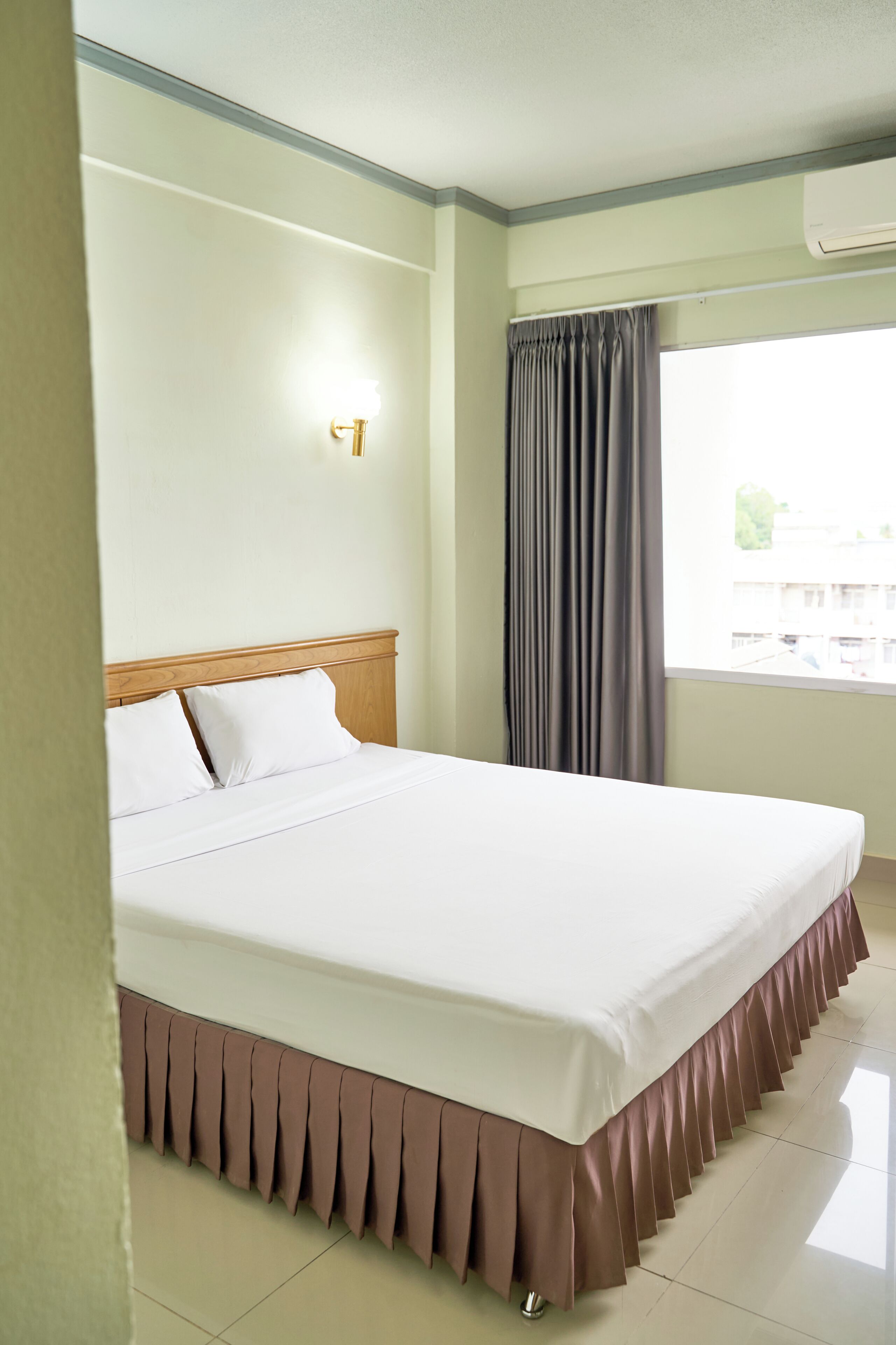 Une chambre d’hôtel avec un lit, une fenêtre avec des rideaux, un climatiseur fixé au mur et un luminaire.