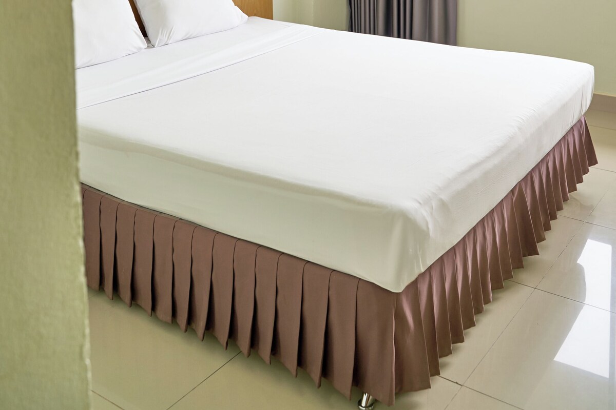 Habitación de hotel con cama, ventana con cortinas, aire acondicionado de pared y lámpara.