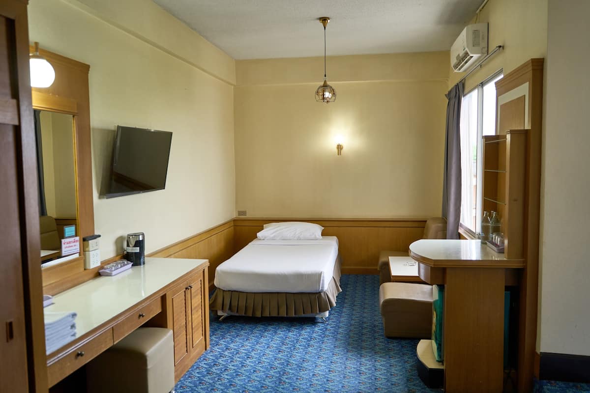 Habitación de hotel con cama, mesita de noche, espejo y un pequeño escritorio con silla.