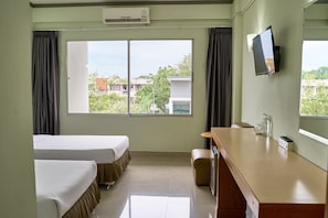 A hotel room with two beds, a desk, a TV, and a window with a view of buildings and trees.
